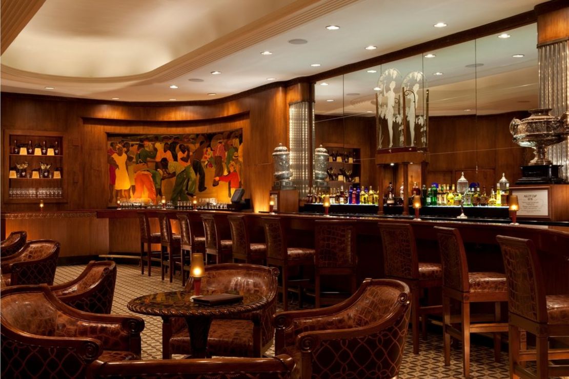 Famous Paul Ninas murals flank the curvaceous walnut-paneled room, furnished with elegant bar stools and plush banquettes. 