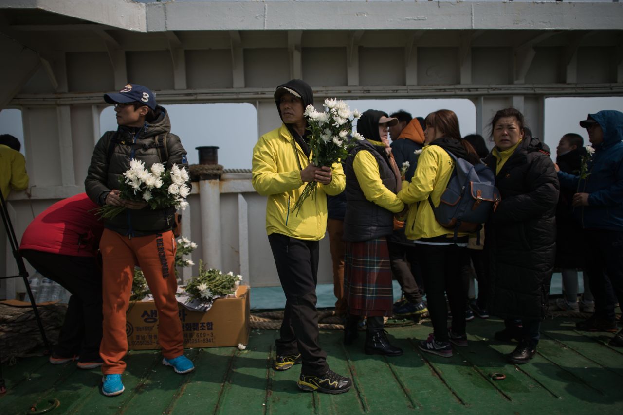 A relative hands out flowers to others on the deck of a boat during a visit to the site of the sunken ferry. More than 100 relatives of victims of South Korea's Sewol ferry disaster tearfully cast flowers into the sea.