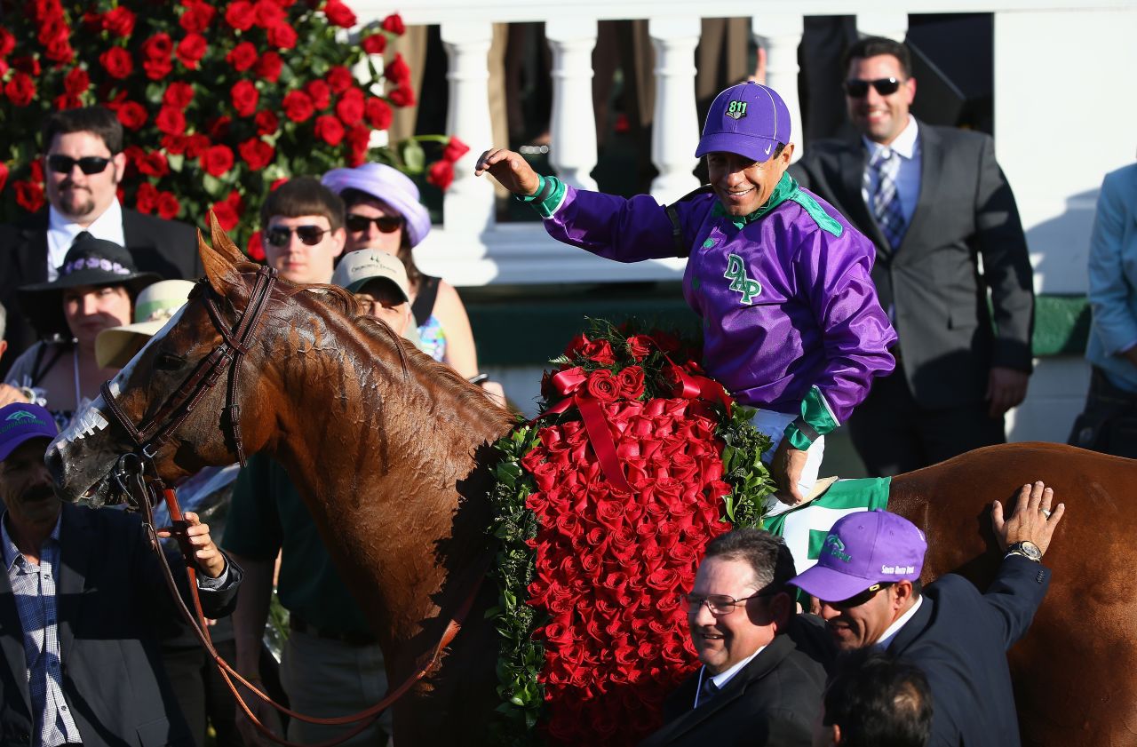 Victor Espinoza celebrates in the winner's circle after riding California Chrome (wearing a traditional victor's blanket of 554 red roses) at the 2014 Kentucky Derby. He will attempt to repeat his win this year with  American Pharoah.  