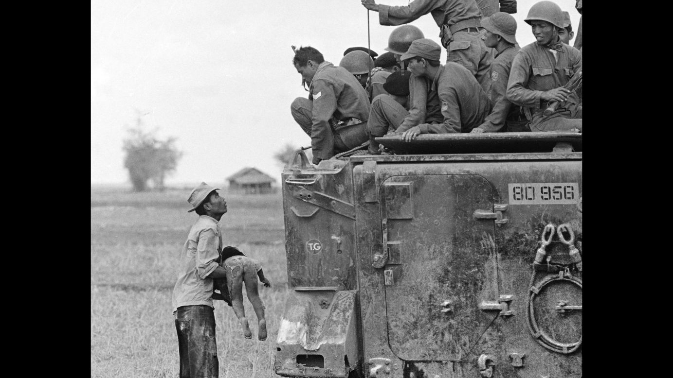 A father holds the body of his child as South Vietnamese Army Rangers look down from their armored vehicle in March 1964. The child was killed as government forces pursued guerrillas into a village near the Cambodian border.