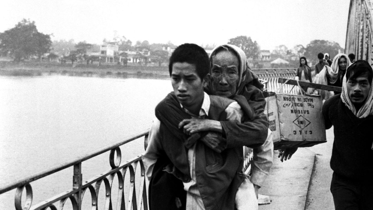 A young refugee carries an elderly woman on his back while crossing a bridge in Hue, Vietnam, in 1968.