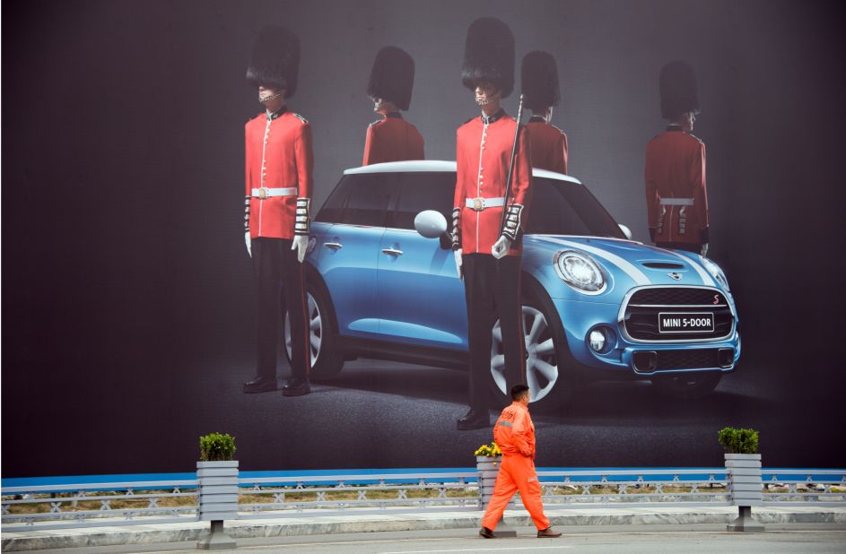 A man walks past a billboard for a Mini 5 door Cooper.