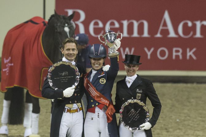 The 29-year-old Dujardin lifts the winner's trophy alongside second placed Dutch rider Edward Gal (L) and Germany's Jessica von Bredow-Werndl in third (R).