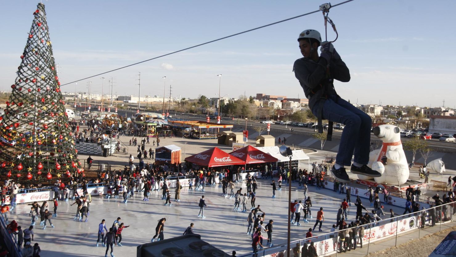 An ice rink in Ciudad Juarez, Mexico, is crowded with skaters as a zip liner passes overhead.