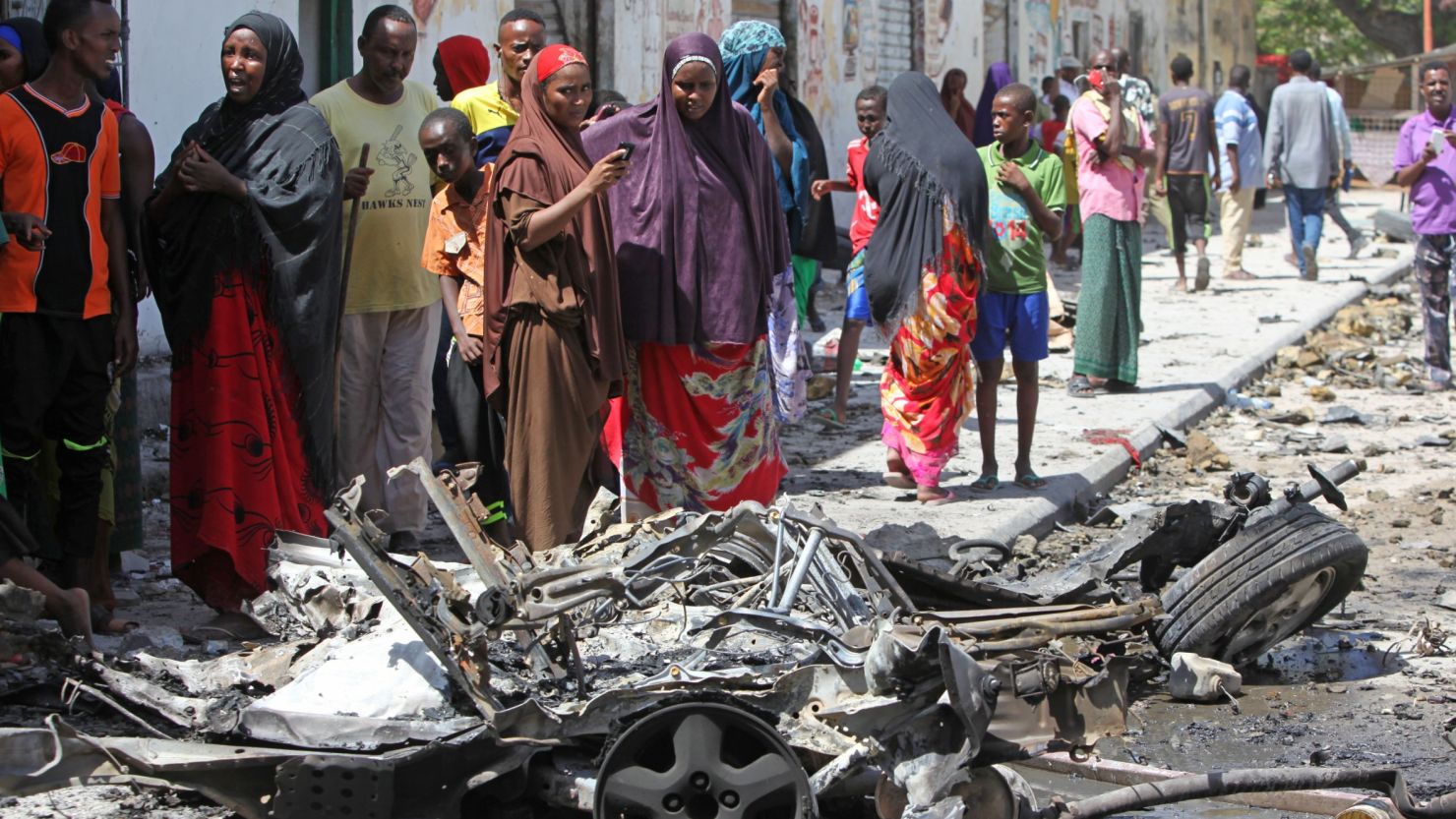 Somalis stand over the wreckage of a car bomb in Mogadishu.