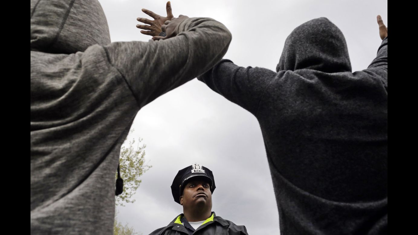A member of the Baltimore Police Department stands guard outside the department's Western District station as men hold their hands up in protest on Wednesday, April 22. <a href="http://www.cnn.com/2015/04/22/us/baltimore-protests-freddie-gray-five-questions/index.html" target="_blank">Protests are gaining steam in Baltimore</a> after a man died from a devastating injury he allegedly suffered while in police custody.