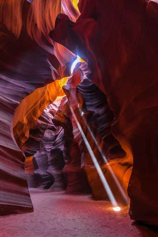 The are only two ways to capture the classic photo of light beams in Upper Antelope Canyon: you can go on a normal tour and hope to get really lucky (nearly impossible), or go on a specific photographic tour on which guides will set you up in specific places at certain times as the beams of light shine into the canyon. They'll also hold back the crowds from normal tours from your shot for a minute or two while you photograph.  
