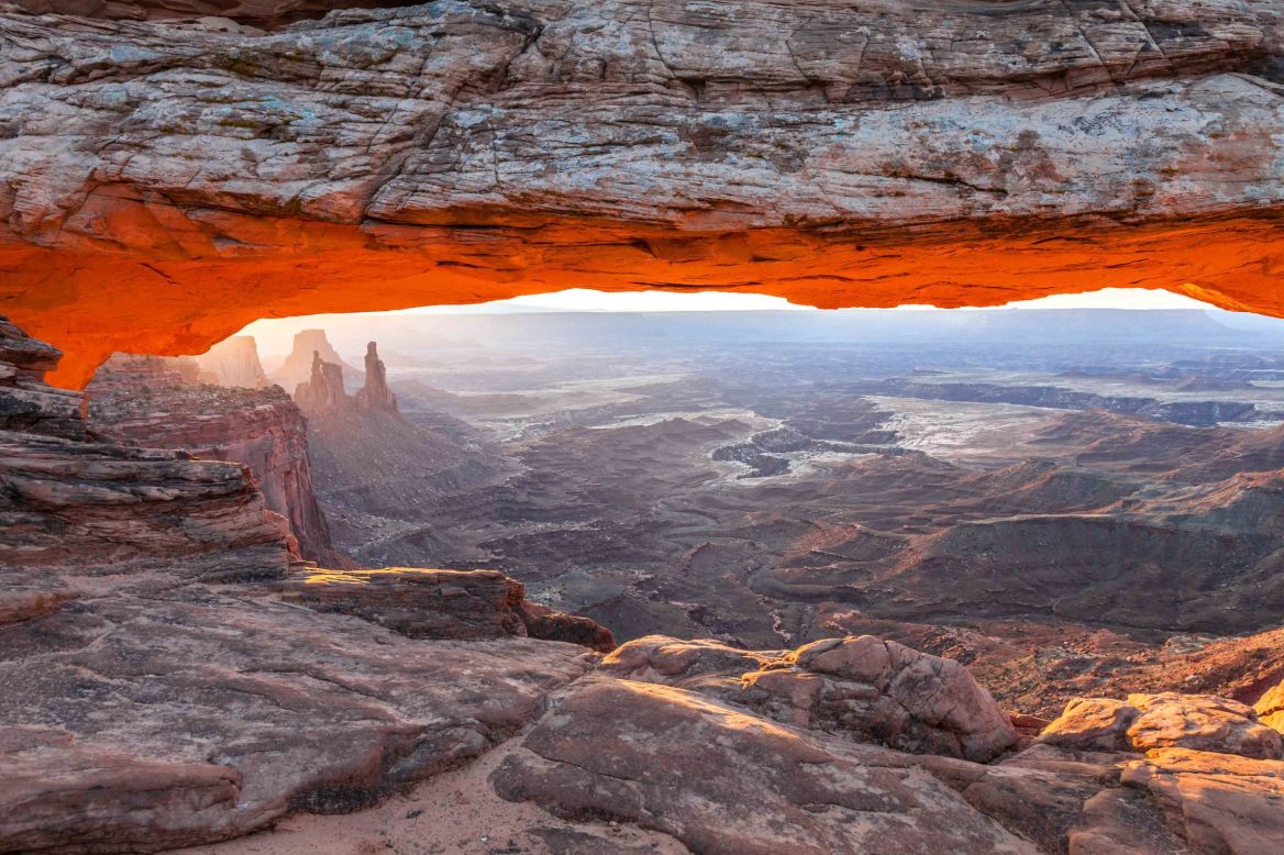 Enjoying the sunrise from Mesa Arch in the Island in the Sky district of Canyonlands National Park is a must-do park experience. Mesa Arch has been made famous in photos thanks to the early morning orange glow on its bottom and the framing it provides for Washerwoman Arch further down the canyon.