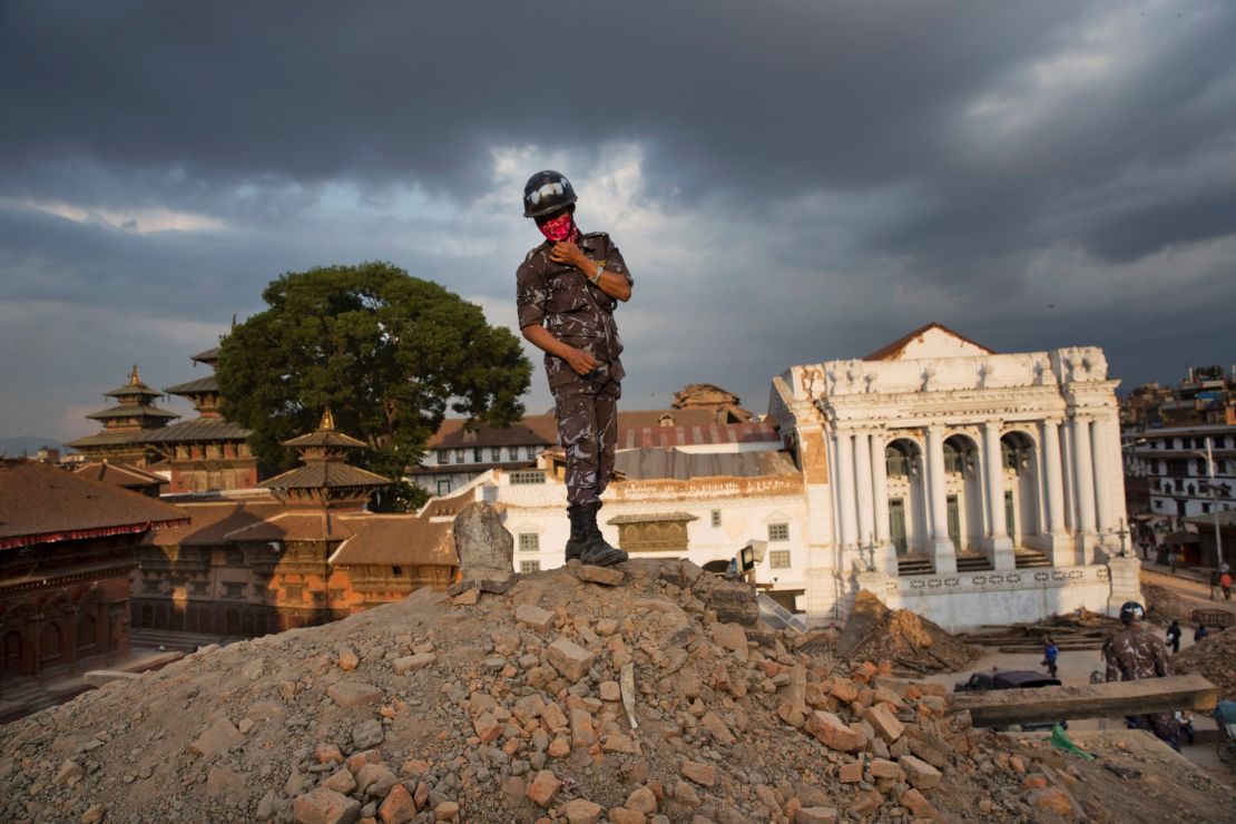 A Nepalese policeman stands atop of a rubble at Basantapur Durbar Square .