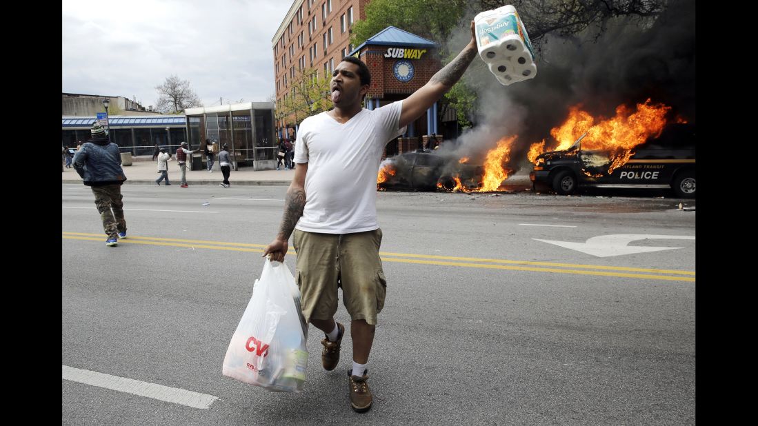 A man carries items from a store as police vehicles burn on April 27.
