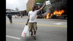 A man carries items from a store as police vehicles burn, Monday, April 27, 2015, after the funeral of Freddie Gray in Baltimore. Gray died from spinal injuries about a week after he was arrested and transported in a Baltimore Police Department van.
