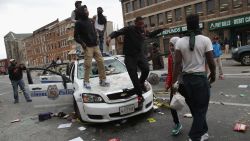 Demonstrators climb on a destroyed Baltimore Police car in the street near the corner of Pennsylvania and North avenues during violent protests following the funeral of Freddie Gray April 27, 2015 in Baltimore, Maryland.