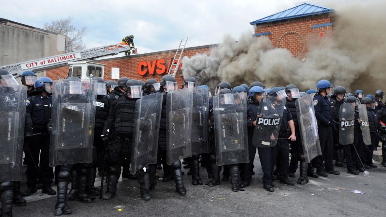 Police form a barrier between protesters and a burning CVS being attended to by firefighters on April 27.