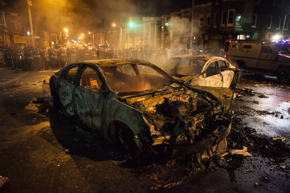 Police retreat from burned-out cars in an intersection on Monday, April 27.
