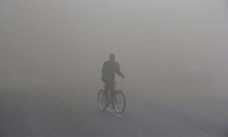 A man rides a bicycle through heavy smoke emitting from a nearby store on fire April 27.