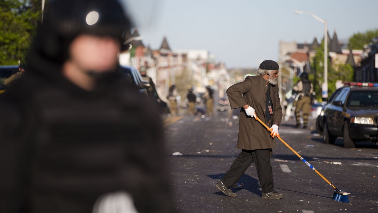 A man sweeps the street as law enforcement officers stand guard on April 28.