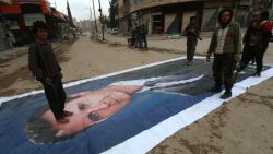 Fighters from a coalition of Islamist forces stand on a huge portrait of Syrian President Bashar al-Assad on March 29, 2015, in the Syrian city of Idlib, the second provincial capital to fall from government control.