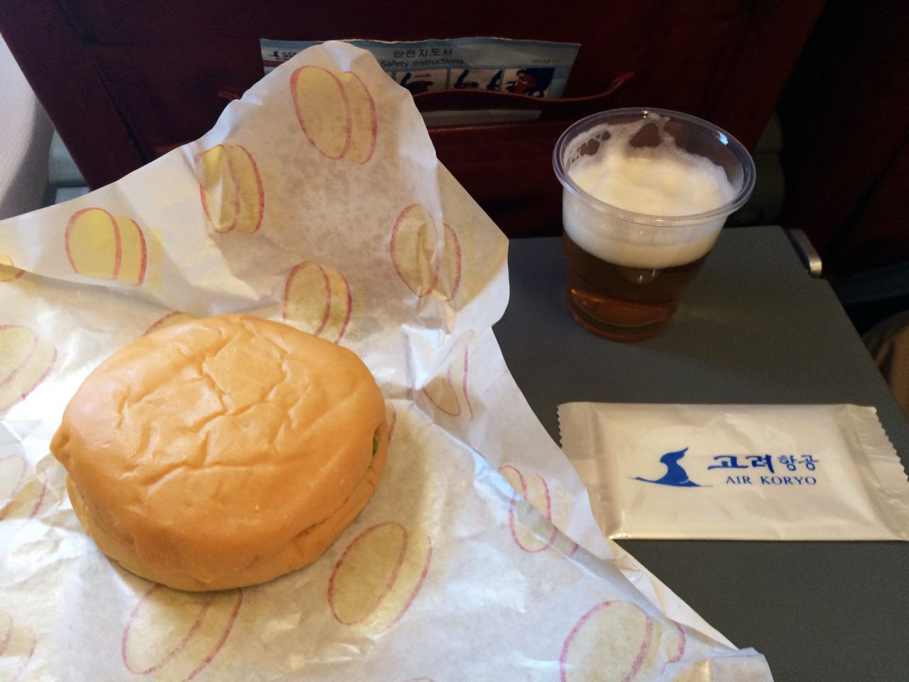The inflight meal consists of a burger and a glass of North Korean beer.  