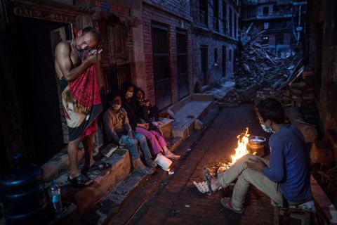 Members of the Tsayana family warm themselves next to a fire outside their damaged house on May 3 in Bhaktapur, Nepal.