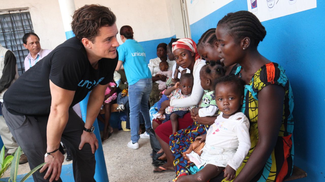 Orlando Bloom speaks with a woman holding her child, at a health center in Monrovia.