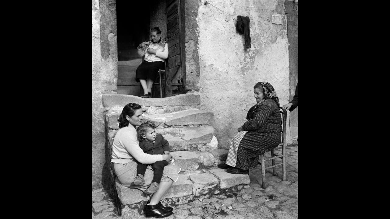 Three generations of women sit and talk on the front steps of a house in Vallecorsa, Italy, in 1968. 