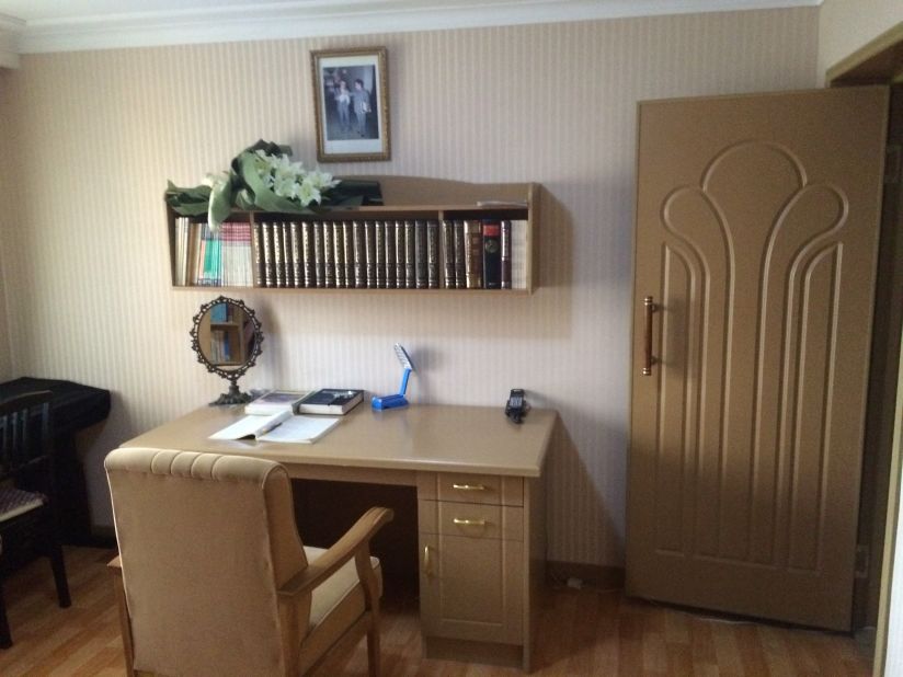 Books are neatly lined up above a desk in the study. There's a lamp for reading and a large padded chair.