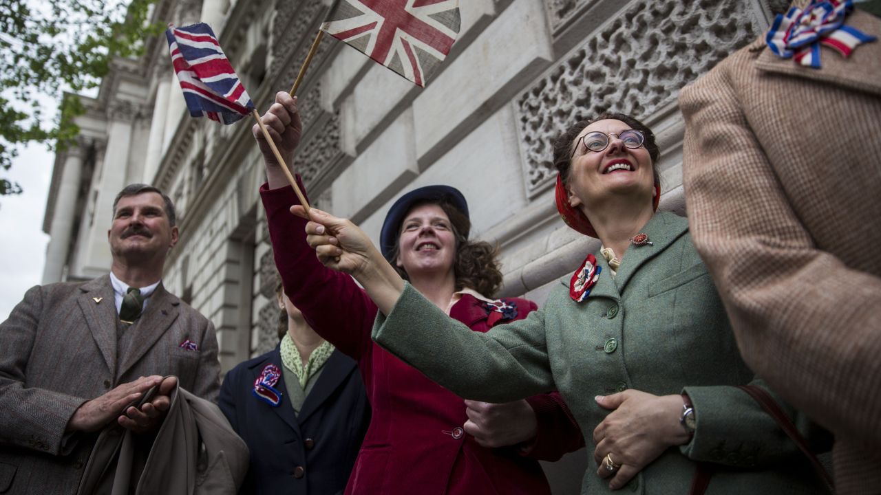 Spectators in London wave flags and wear World War II-era clothing.