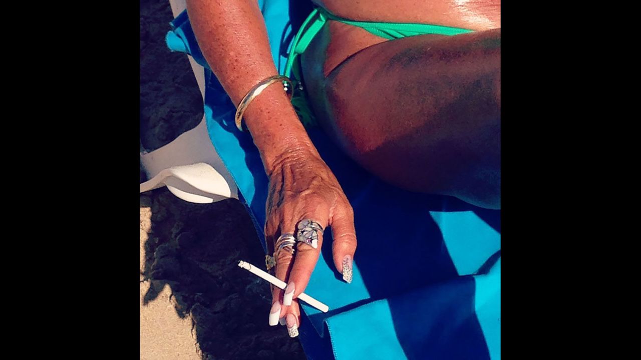 A woman smokes a cigarette on the beach.