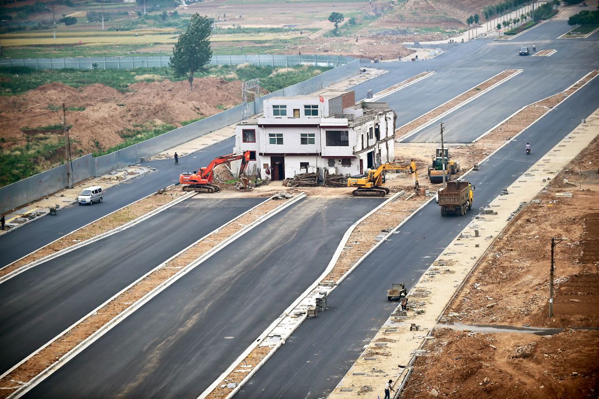 A three-story house stands in the middle of a newly built road in China's Henan province on May 16, 2015. Construction was put to a halt as the owner refused to move because of a dispute about compensation. Like a nail that refuses to be hammered down, the dwelling is one of many "nail houses" that have sprung up in China as some homeowners resist development of their land or hold out for more money. According to construction workers, the owner is still living inside the house even though the rest of the road is complete.