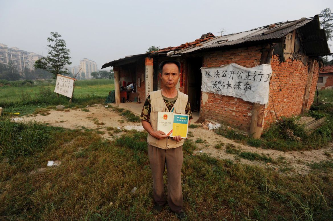 In a picture taken on June 6, 2010, Chinese farmer Yang Youde poses with a copy of China's Property Law on his farmland in front of his house on the outskirts of Wuhan, in central China's Hubei province. Yang uses improvised cannons, which are made out of a wheelbarrow, pipes and fire rockets, to defend his fields against property developers who want his land.