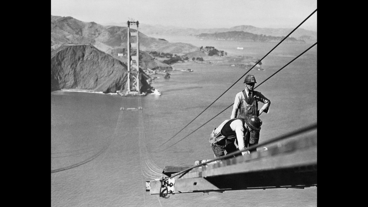 Bridge workers build a catwalk that connects the towers at both sides of the strait so they can attach the suspension cables to hold up the bridge. Workers on the bridge were buffeted by high winds and faced constant fears of plummeting to their deaths.