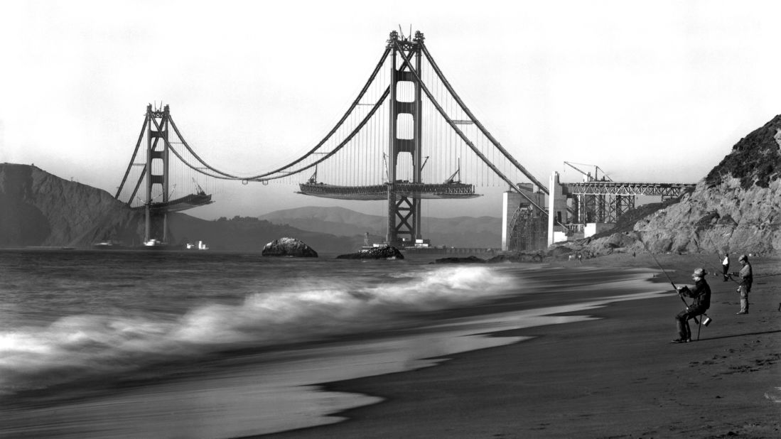 Fishermen on Baker Beach enjoy the view of the Golden Gate Bridge under construction. Work on the bridge began on January 5, 1933, and lasted four years and four months. The span is painted a distinctive color named "international orange."