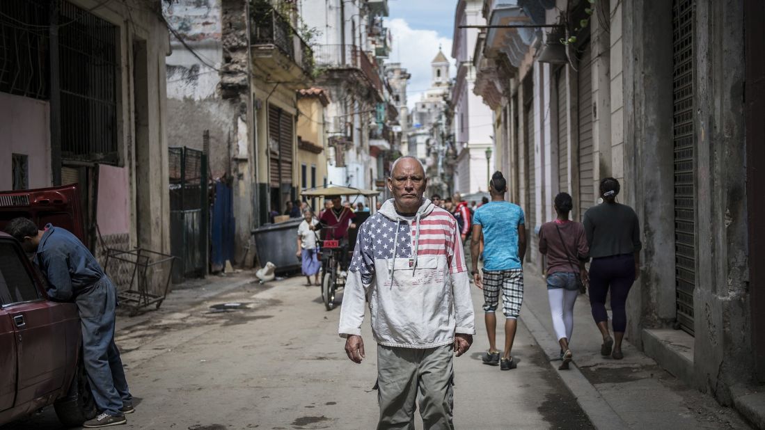 A man wearing an American flag sweatshirt walks through a street in Havana in February.