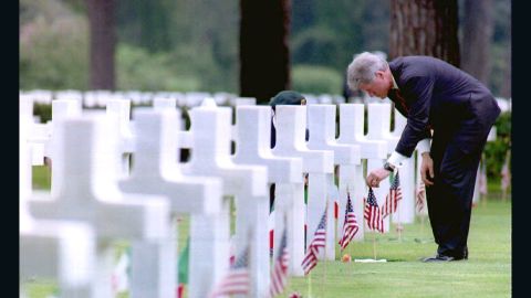 Then-President Bill Clinton adjusts a U.S. flag at the grave of Army Lt. Robert Waugh as he visits the Sicily-Rome American cemetery in June, 1994. 