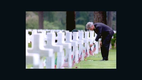 Then-President Bill Clinton adjusts a U.S. flag at the grave of Army Lt. Robert Waugh as he visits the Sicily-Rome American cemetery in June, 1994.