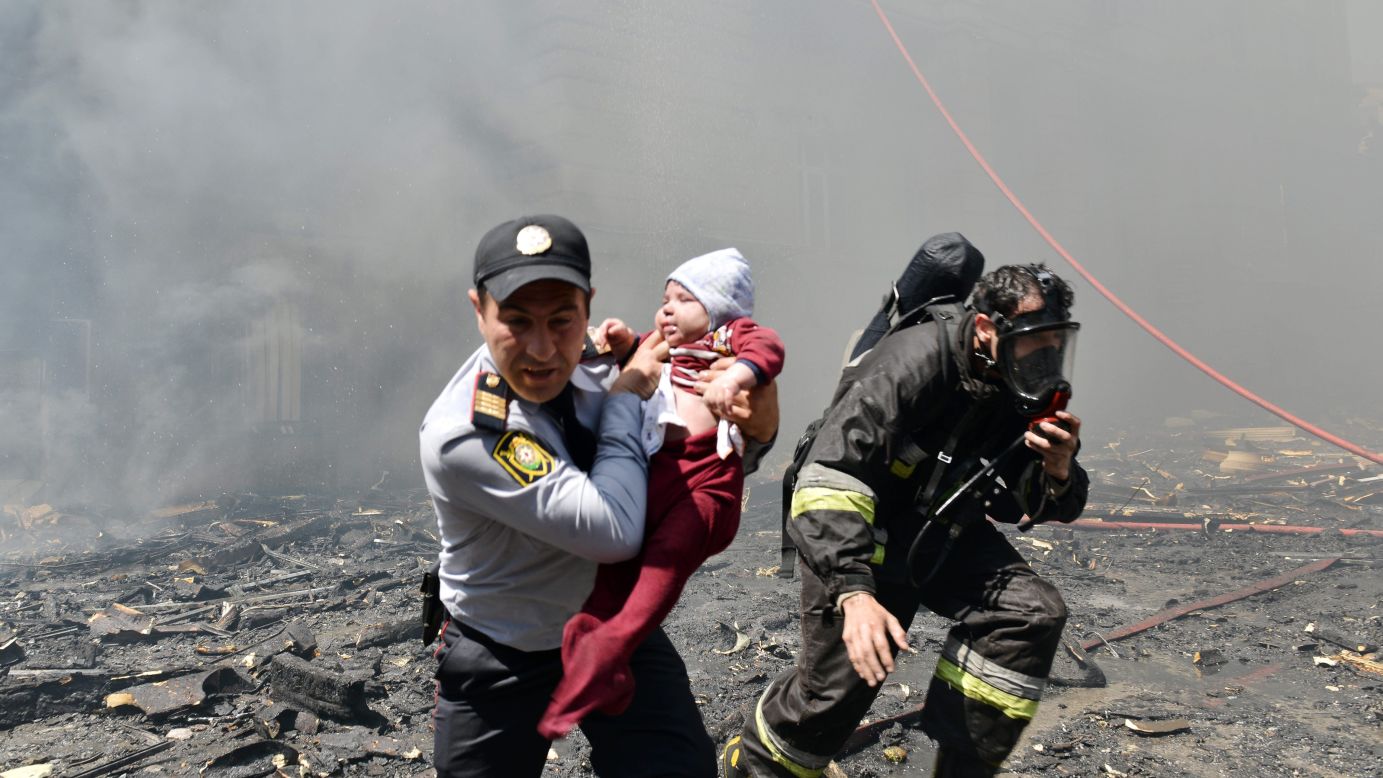A police officer and a firefighter help a child from an apartment building fire in Baku, Azerbaijan, on Tuesday, May 19. Officials said at least 16 people died and more than 50 were injured in the 16-story building.