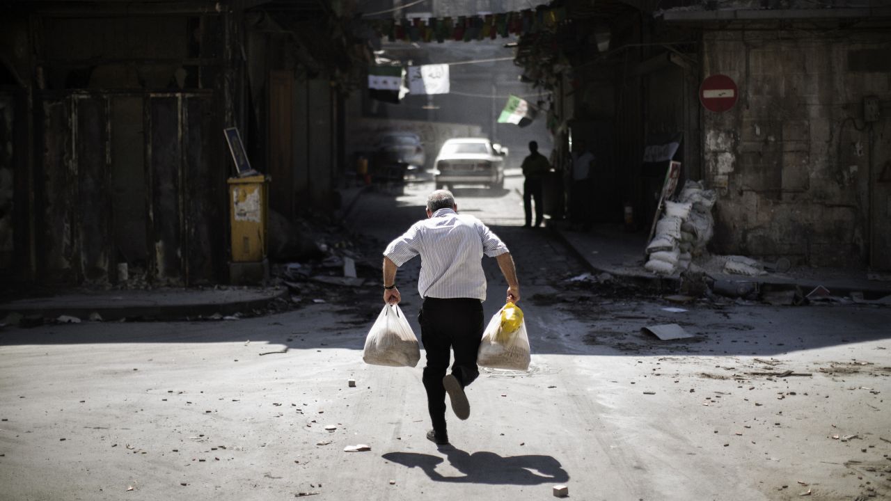 A Syrian man carrying grocery bags dodges sniper fire in Aleppo as he runs through an alley near a checkpoint manned by the Free Syrian Army on September 14, 2012.
