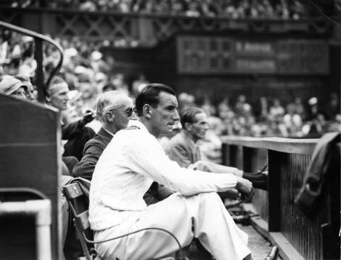 The 1936 champion Fred Perry takes a seat on a courtside bench to enjoy the match between Donald Budge and Bunny Austin.