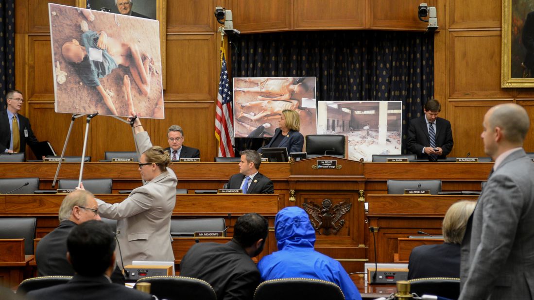 Photographs of victims of the Assad regime are displayed as a Syrian army defector known as "Caesar," center, appears in disguise to speak before the House Foreign Affairs Committee in Washington. The July 31, 2014, briefing was called "Assad's Killing Machine Exposed: Implications for U.S. Policy." Caesar, apparently a witness to the regime's brutality, smuggled more than 50,000 photographs depicting the torture and execution of more than 10,000 dissidents. CNN cannot independently confirm the authenticity of the photos, documents and testimony referenced in the report.