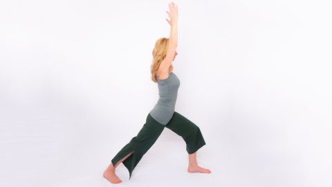 Santas demonstrates Warrior One, a basic standing yoga pose that lengthens the upper body while stretching hip flexors and stabilizing the low back. From standing, step back into a lunge but drop your back heel and point your toes out 45 degrees. Keep your back leg straight with your forward knee flexed above your ankle. Lift your arms overhead, shoulder-distance apart. Hold for three to five long, deep breaths. Repeat on the other side.
