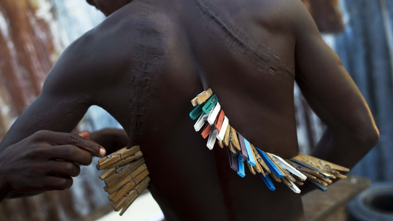 A man helps his friend to remove clothespins from his back while they play dominoes in Port-au-Prince, Haiti, on Friday, May 29. Their rules stipulated that a player who loses a game must place clothespins on his body. The pins could only be removed when another player lost.