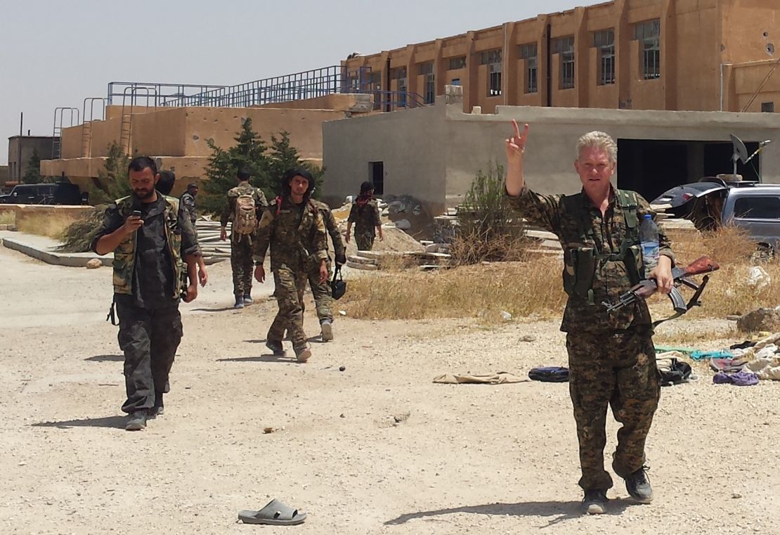 Enright, right, wears the military uniform of Kurdish fighters and flashes a victory sign last month in Syria.