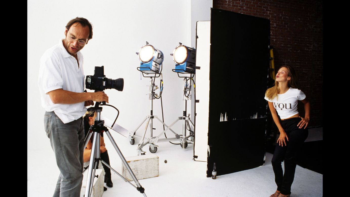 Photographer Kim Knott stands at his camera addressing an assistant as Moss strikes a pose during a 1995 shoot in New York City.