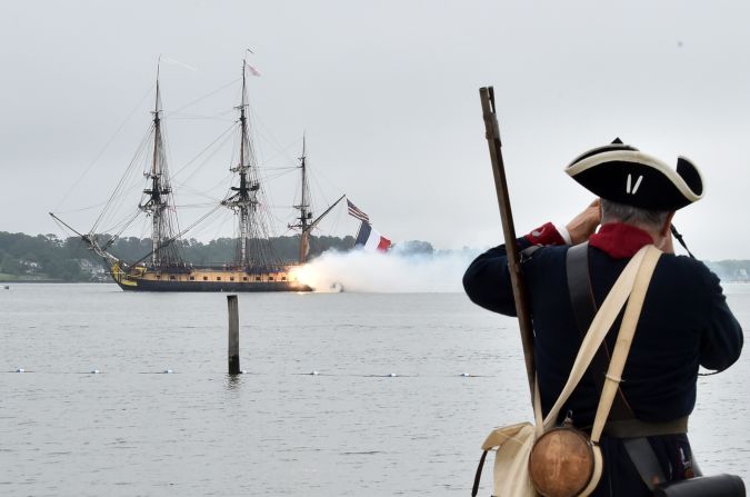 A man dressed in period costume watches as the vessel gives a 21 gun salute in the Yorktown City Harbor.