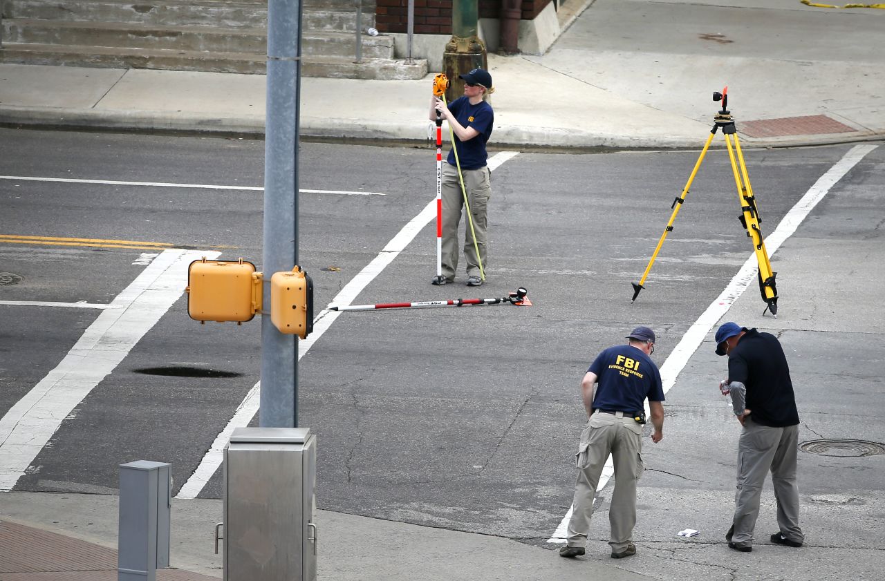 FBI evidence response team members look down at a piece of marked evidence on the street in front of Dallas police headquarters.
