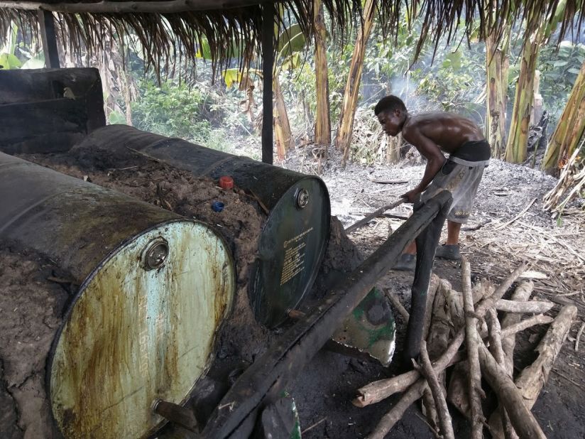 A  young man puts more wood on the fire to heat drums of fermented palm sap and evaporate the alcohol.
