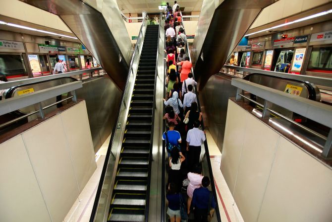 An escalator inside the Raffles Place MRT station during rush hour, at the central business district area.