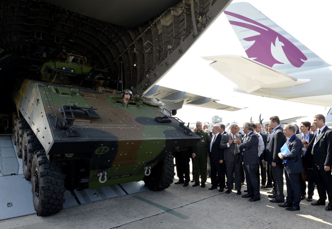 French officials look on an armored military vehicle is unloaded from the Airbus A400M "Grizzly" transporter plane at the Paris Airshow. 