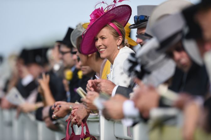 A female racegoer unknowingly takes center stage amid her male counterparts as she leans on a barrier to watch the racing.