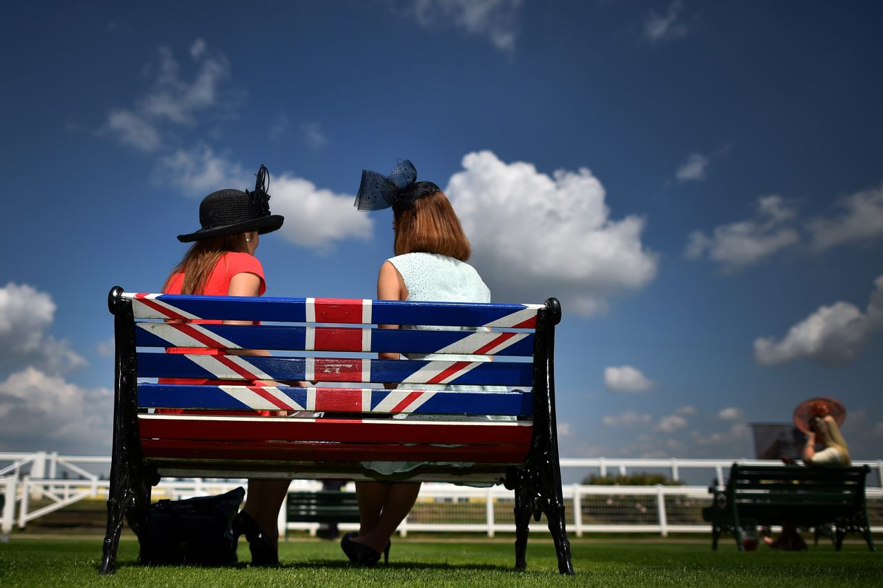 Two female racegoers take time out from the day's action on a Union Jack bench under blue skies.